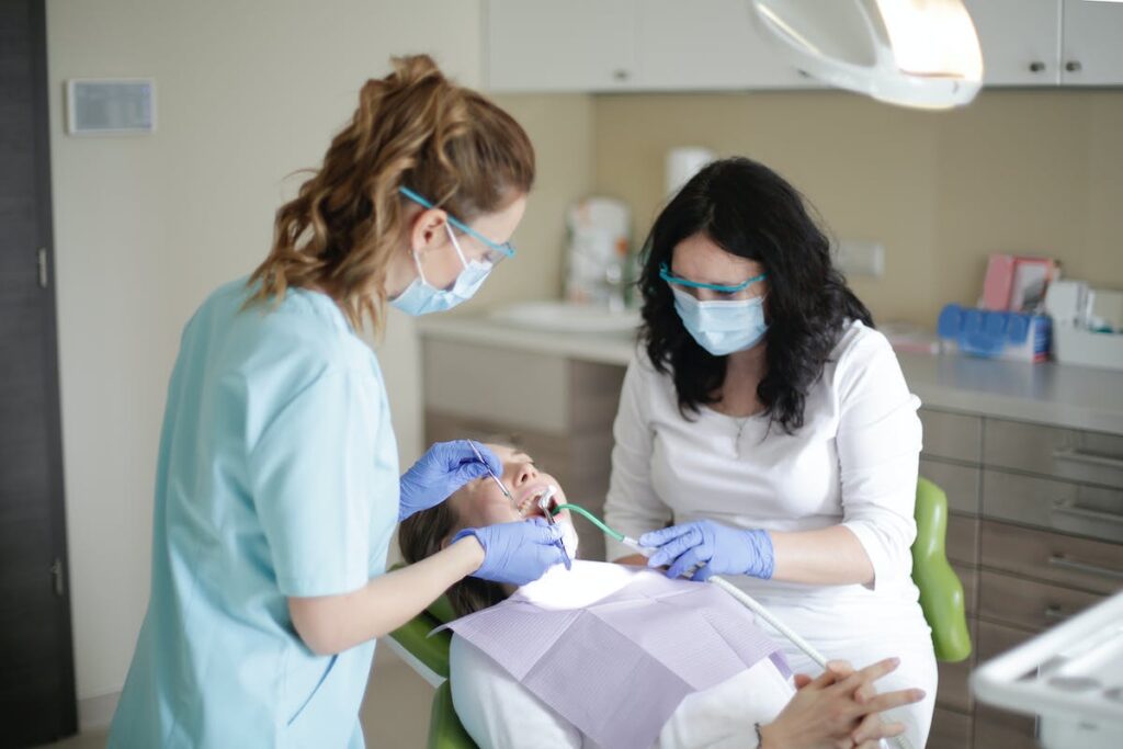 Female dentist in mask and assistant using dental tools for examining teeth of female patient