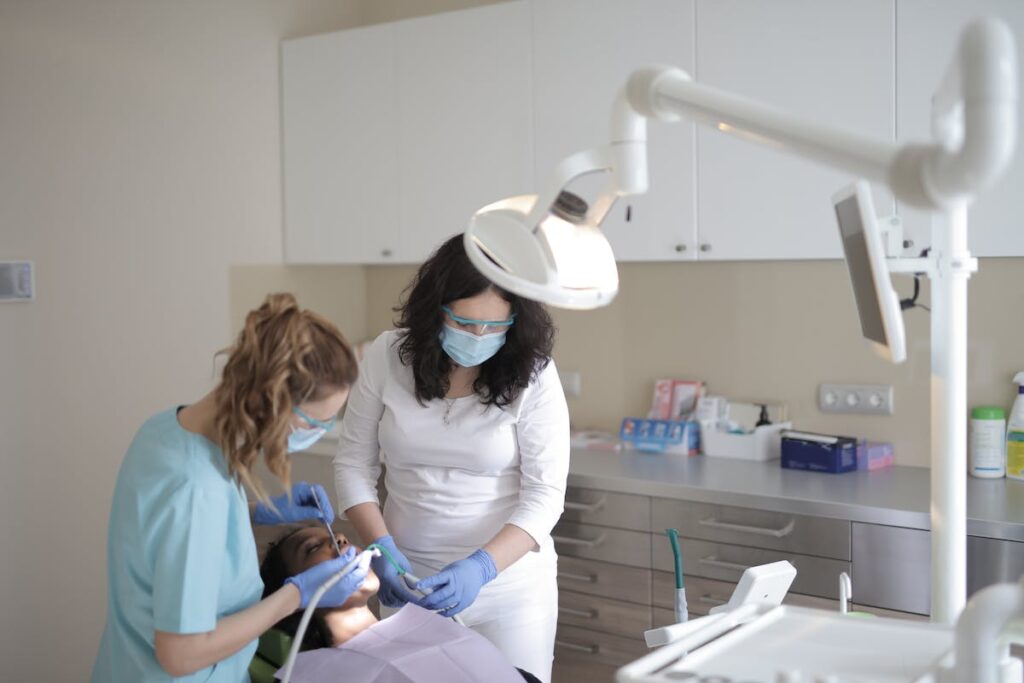 Female dentists treating teeth of patient in modern clinic