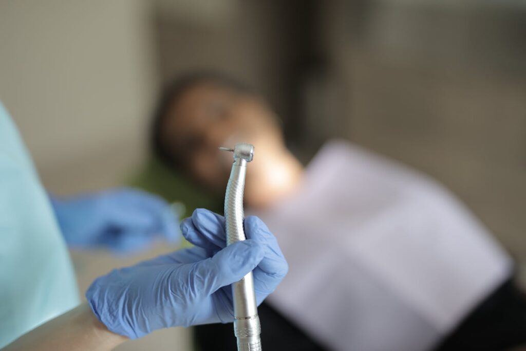 Unrecognizable crop dentist holding drill while treating patient in clinic