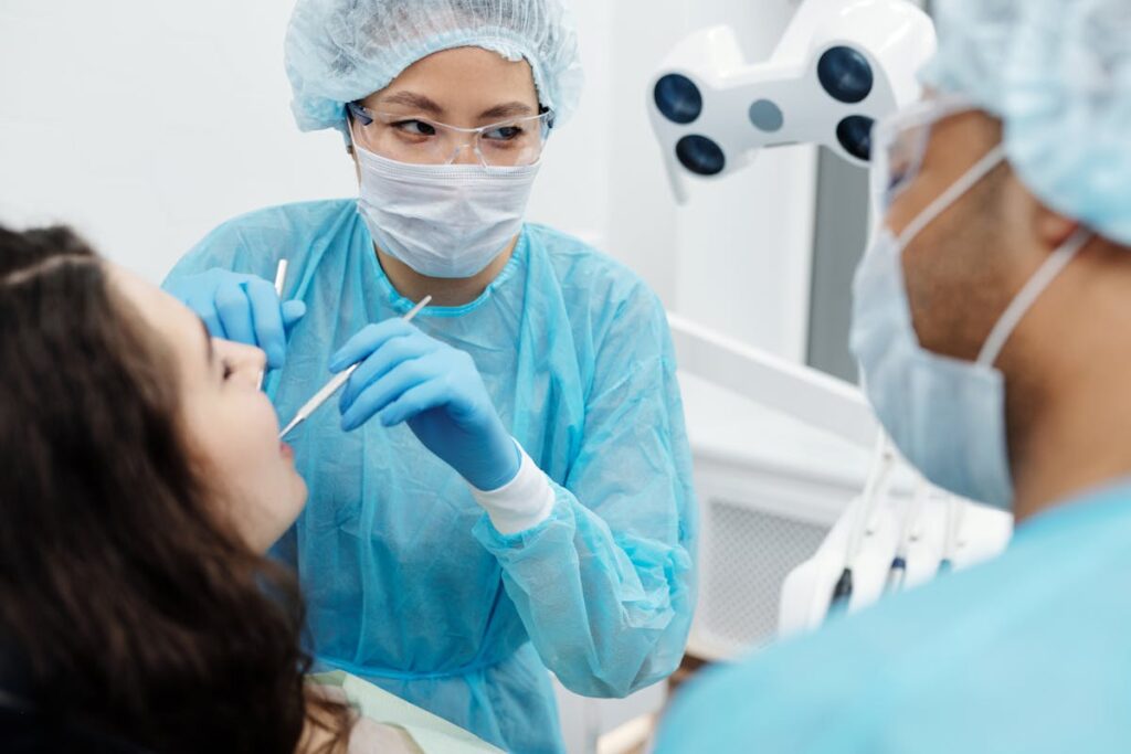 Woman in Blue Long Sleeve Scrub Suit Checking the Patient's Teeth