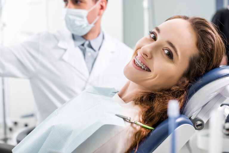 selective focus of beautiful woman in braces during examination of teeth near dentist