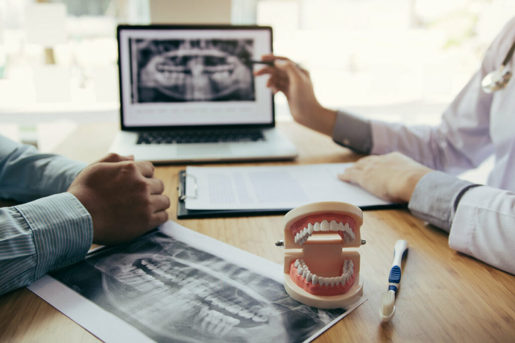 Dentists are discussing dental problems at report x-ray image on laptop screen to patients.